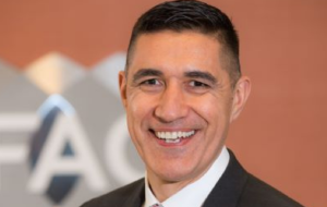 man smiling in suit, ifac logo in background