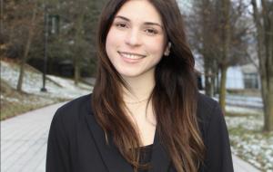 A woman in a black blazer standing smiling at the camera