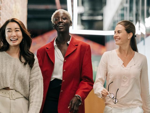 Three women smiling as they walk down the hallway of an office