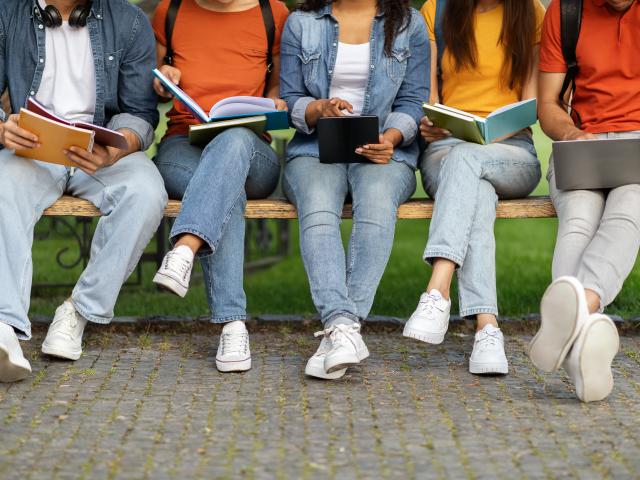 Jeans clad legs of college students sitting on a bench