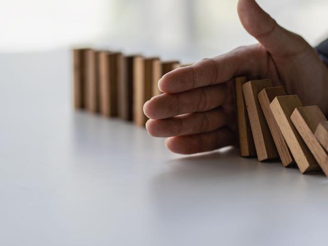 A man's hand stops wooden dominoes from falling into each other on a white table.