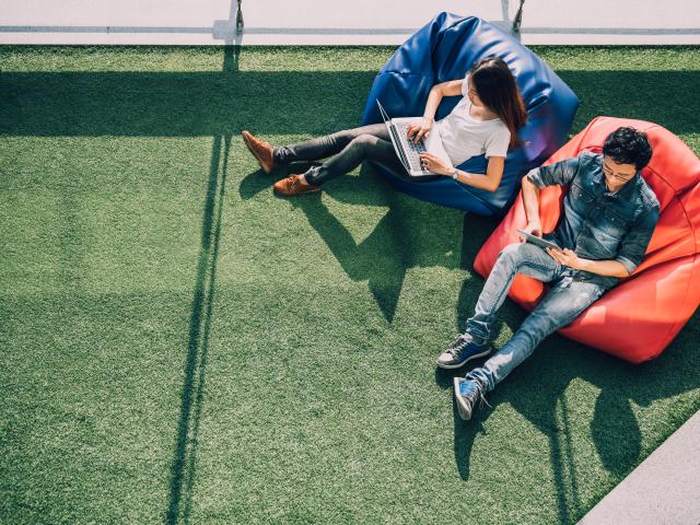 Two young people sit on blue and orange beanbags on green astroturf. The photo is taken from above.