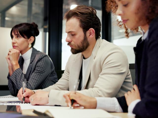 Three people sitting at a table taking notes during a meeting