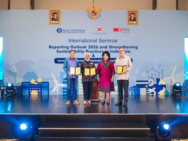 A group of four standing onstage, holding documents