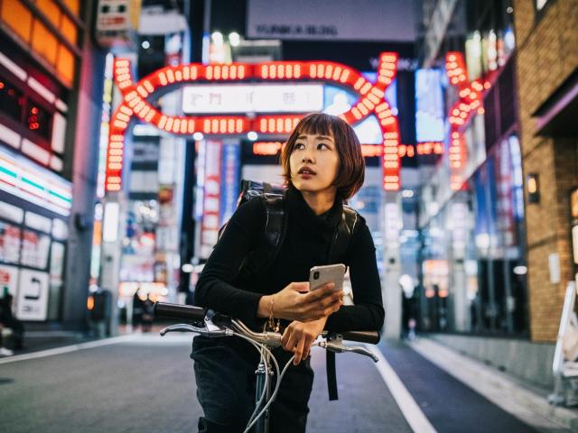 A woman on a bike with a neon-lit city background