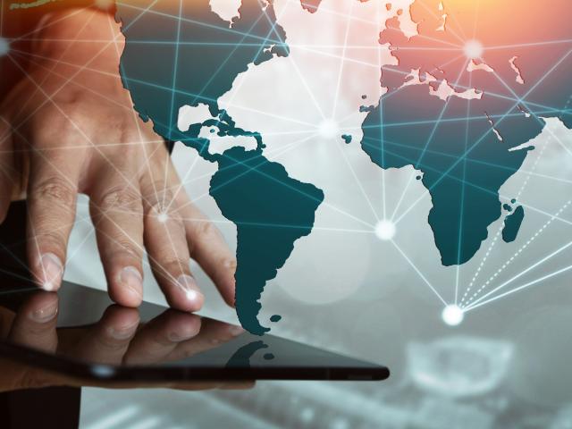 A hand using a tablet with a global map in the background