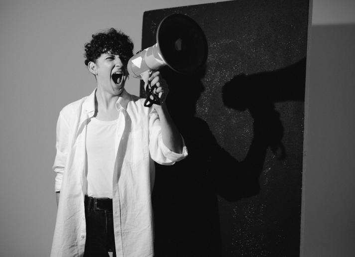 A young person stands with their mouth open and a megaphone in front of their face in black and white