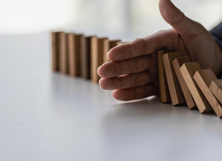 A man's hand stops wooden dominoes from falling into each other on a white table.