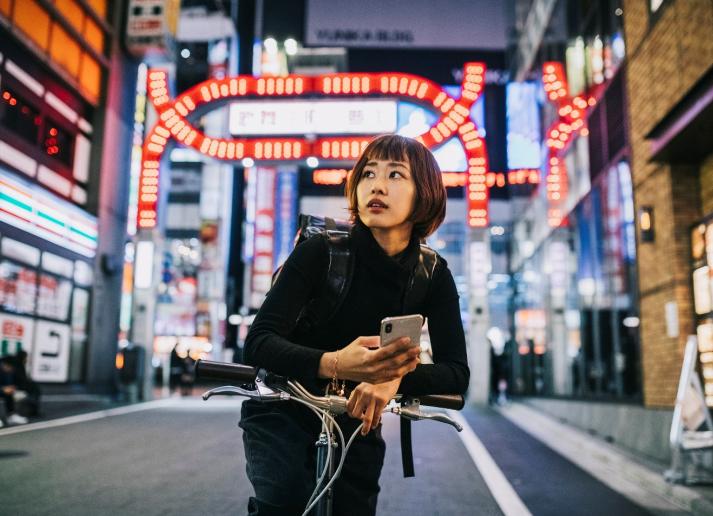A woman on a bike with a neon-lit city background