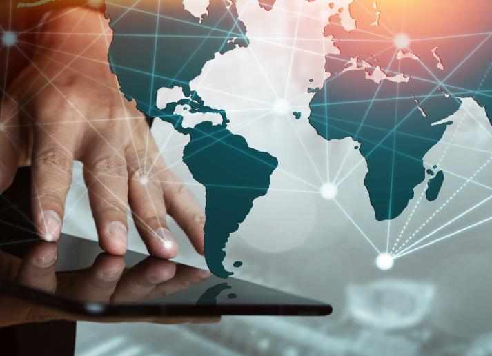 A hand using a tablet with a global map in the background