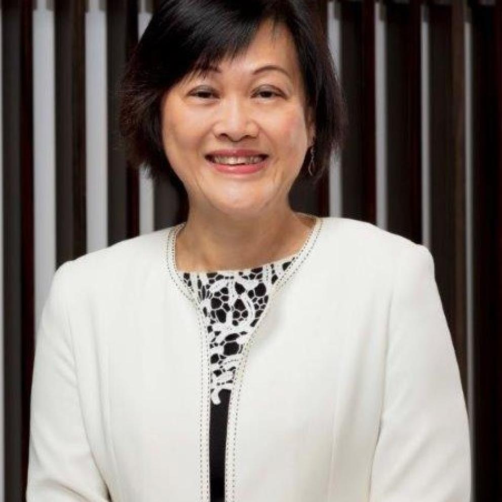May Tan is standing wearing a white jacket and smiling