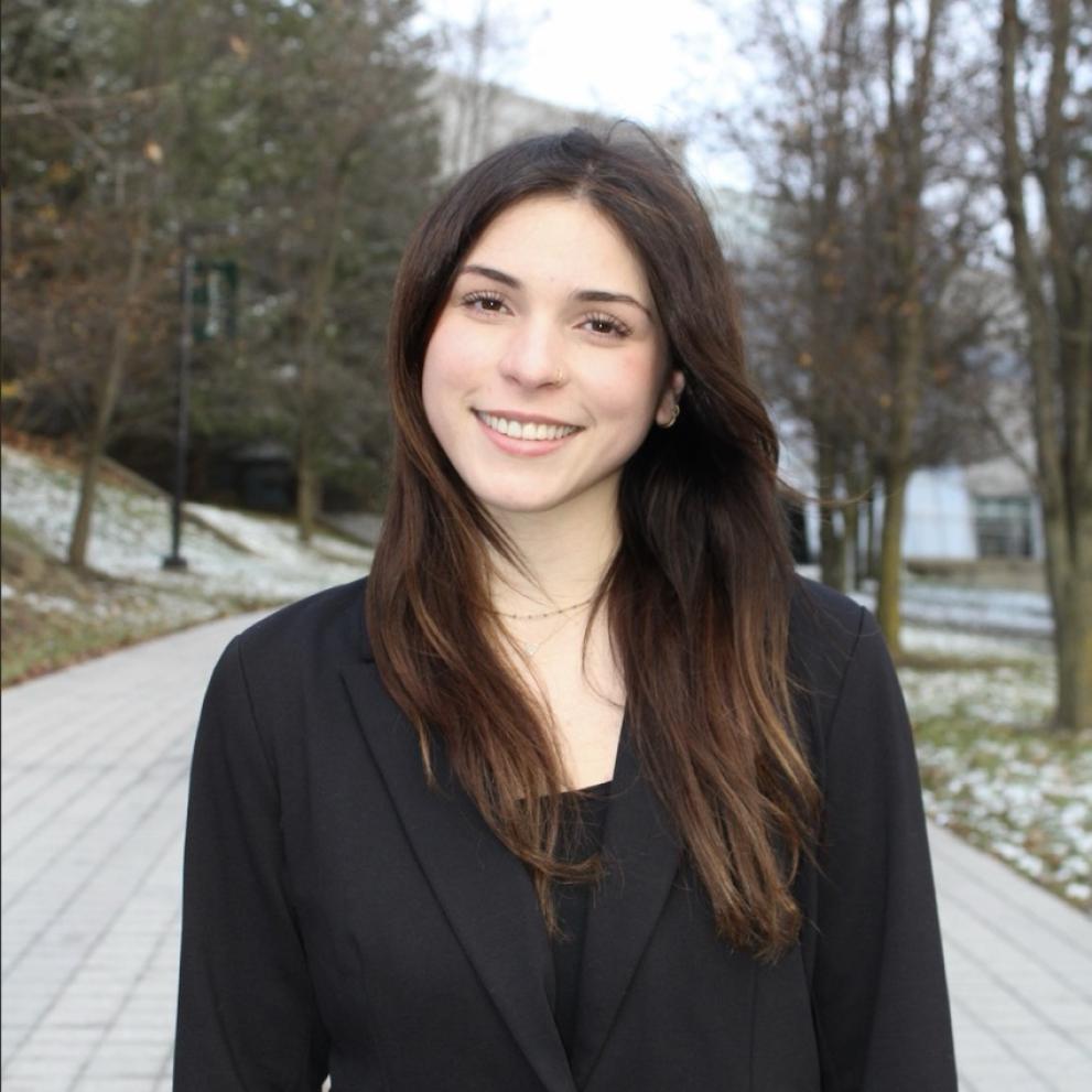 A woman in a black blazer standing smiling at the camera