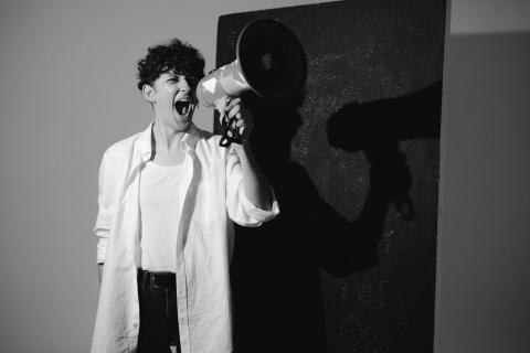A young person stands with their mouth open and a megaphone in front of their face in black and white