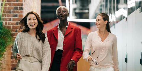 Three women smiling as they walk down the hallway of an office