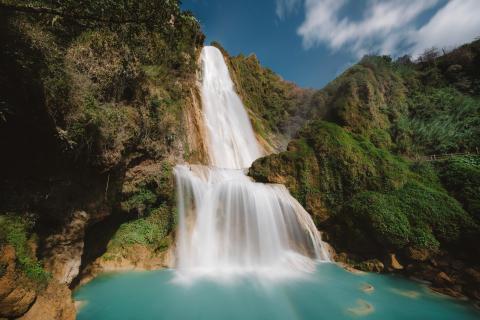 A waterfall emptying into a blue pool. surrounded by a forest