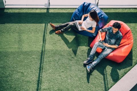 Two young people sit on blue and orange beanbags on green astroturf. The photo is taken from above.