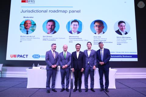 Speakers on a panel standing in front of a slide on stage